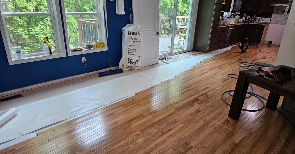 Wood floor installation underway with underlayment, partially laid boards and tools visible